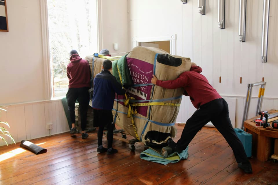 Movers wheeling blanket-wrapped furniture across a wooden floor