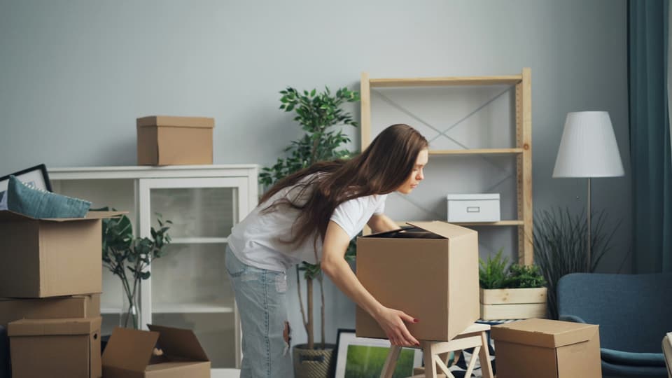 A woman lifting a packed moving box in a room full of boxes