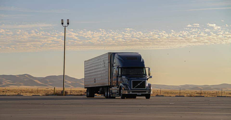 A tractor-trailer truck on an open highway at sunset